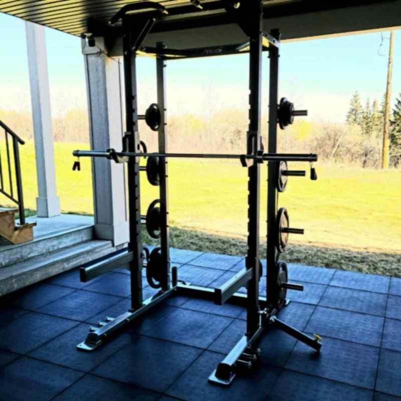 Gym squat rack on a patio with a view of a grassy area and trees.