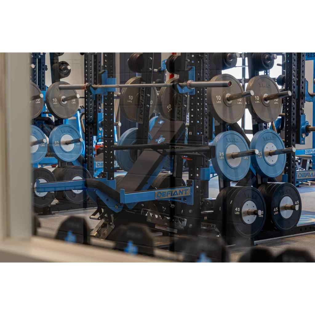 Gym weight rack with barbell and weights, featuring the brand 'Defiant'.